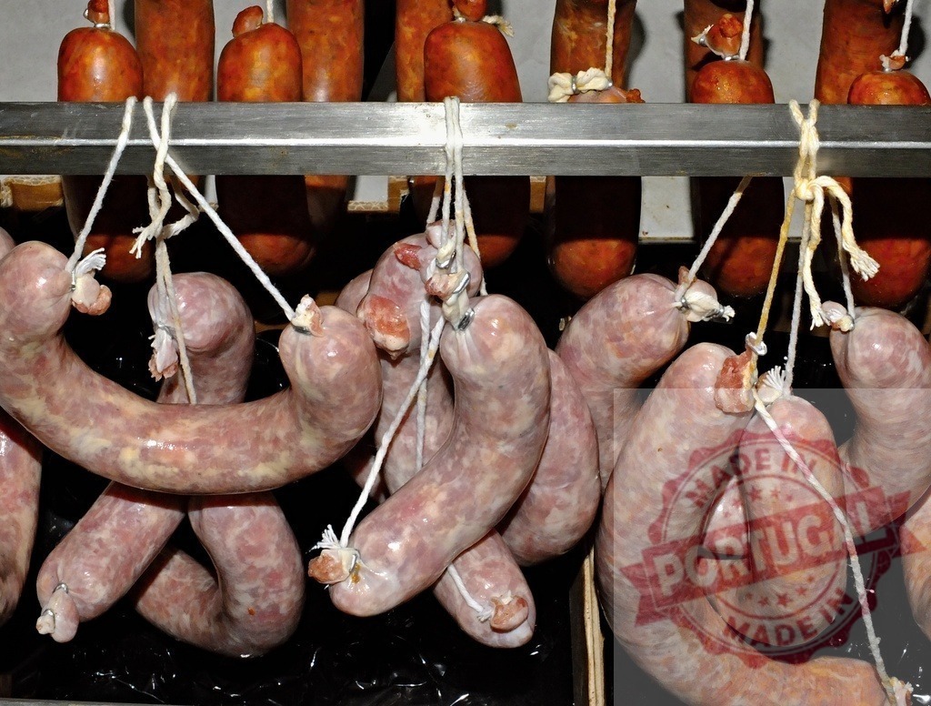 Fresh raw sausages hanging for curing in butcher's shop | Raw sausages hanging from racks, preparing for curing process in a meat storage facility - Realized with Pictrs.com