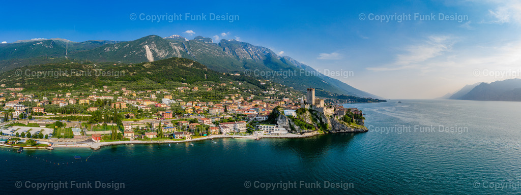 Drohnenpanorama von Malcesine am Gardasee – Venetien, Italien | Ein weites Drohnenpanorama zeigt Malcesine am Gardasee mit der markanten Burg Castello Scaligero direkt am Ufer. Die Kombination aus Altstadt, Bergkulisse und ruhigem Seewasser wirkt gleichzeitig elegant und urlaubsleicht.