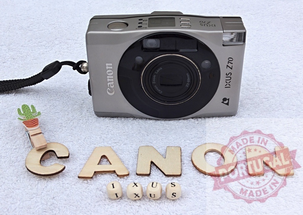 Canon IXUS Z70 compact film camera with wooden letters | Canon IXUS Z70 vintage compact film camera on white background with wooden letters - Realized with Pictrs.com