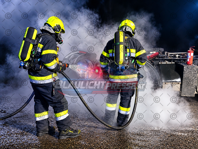 Lkw-Brand – Feuerwehreinsatz bei einem brennenden Lastkraftwagen (Symbolbild) | Symbolbild eines Lkw-Brandes bei Nacht: Zwei Feuerwehrleute unter schwerem Atemschutz bekämpfen einen Brand an einem Lastkraftwagen. Dichter Rauch, Löschwasser und die Beleuchtung der Einsatzstelle sorgen für eine realistische Einsatzatmosphäre. Das Bild eignet sich für die Berichterstattung über Lkw-Brände, Fahrzeugbrände und Feuerwehreinsätze in Print- und Onlinemedien. Das Foto wurde vom Fotografen aufgenommen und mithilfe von KI optimiert. Das ursprüngliche Fotomotiv stammt aus einer realen Aufnahme. - Realisiert mit Pictrs.com