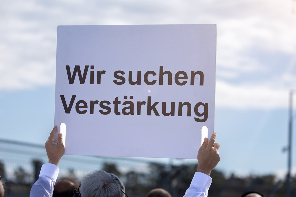 WIR SUCHEN VERSTÄRKUNG Schild | (Fotomontage) Ein Schild mit dem Text WIR SUCHEN VERSTÄRKUNG wird in die Höhe gehalten - Realisiert mit Pictrs.com
