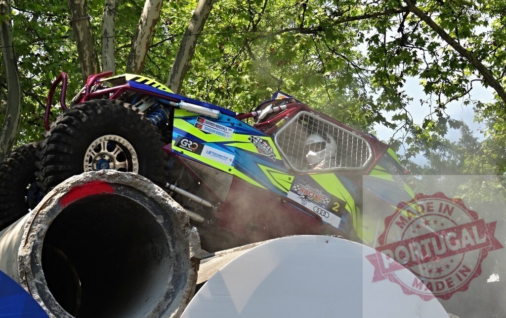 Buggy climbing concrete pipes during an off-road race | Off-road racing vehicle driving over concrete pipes during a competition, kicking up dust - Realized with Pictrs.com