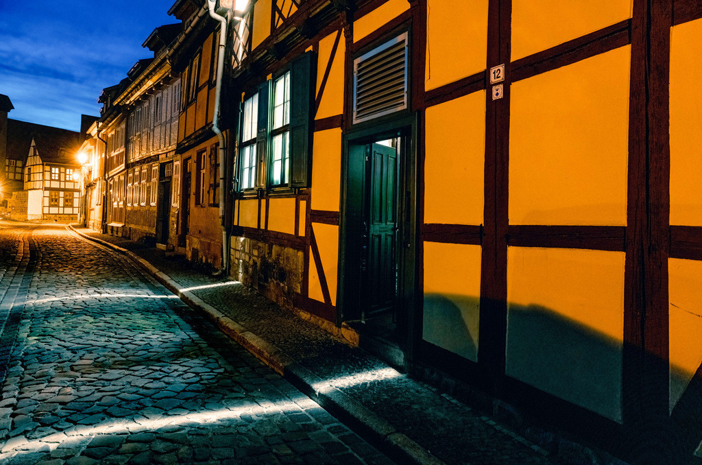 Urige beleuchtete Straße Szene mit Fachwerkhäusern in Quedlinburg  | Das Bild zeigt eine historische Straße in der Altstadt von Quedlinburg. Quedlinburg ist bekannt als eine der größten Fachwerkstädte Deutschlands mit über 2000 Fachwerkhäusern. Die Stadt gilt als Flächendenkmal und gehört zum UNESCO-Weltkulturerbe. Die Szene fängt die besondere Atmosphäre der historischen Gassen ein, die oft als Kulisse für Filmproduktionen dienen. Die Architektur umfasst Gebäude aus sechs Jahrhunderten, darunter Häuser aus der Renaissance und dem Barock.  - Realisiert mit Pictrs.com