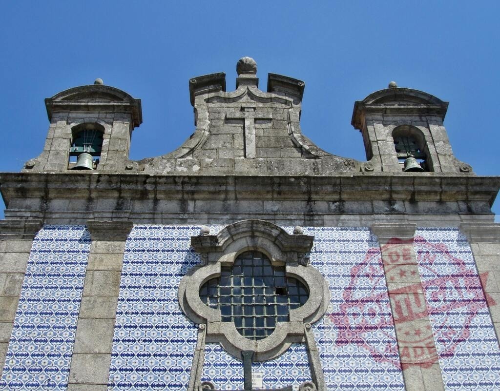 São Bento da Vitória convent church facade with azulejos. Portugal - Norte | Ornate church facade featuring traditional Portuguese azulejos, bell towers, and a cross against a blue sky - Realized with Pictrs.com