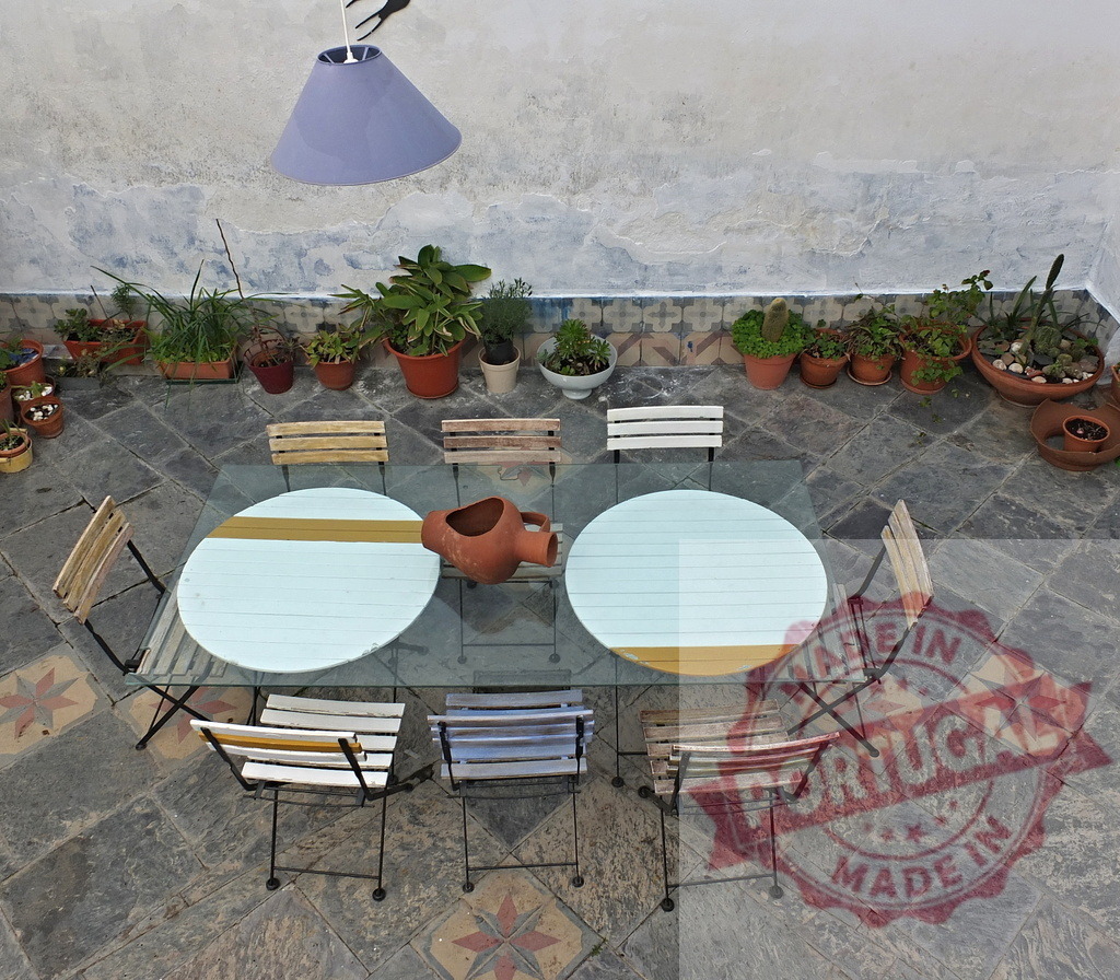 Outdoor dining area with rustic patio furniture and potted plants | Overhead view of a charming Mediterranean courtyard patio with glass table, chairs, and many green plants - Realized with Pictrs.com