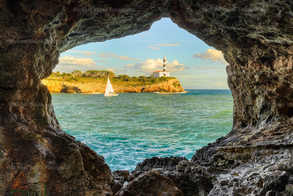 Blick durch einen Felsbogen in Portocolom auf Mallorca | Durch den Felsbogen von Portocolom öffnet sich der Blick auf den ikonischen Leuchtturm – eingerahmt von warmem Fels, vor dem türkisblauen Mittelmeers. Ein natürlicher Rahmen, ein perfekter Moment und ein Stück mallorquinische Küstenmagie. - Realisiert mit Pictrs.com