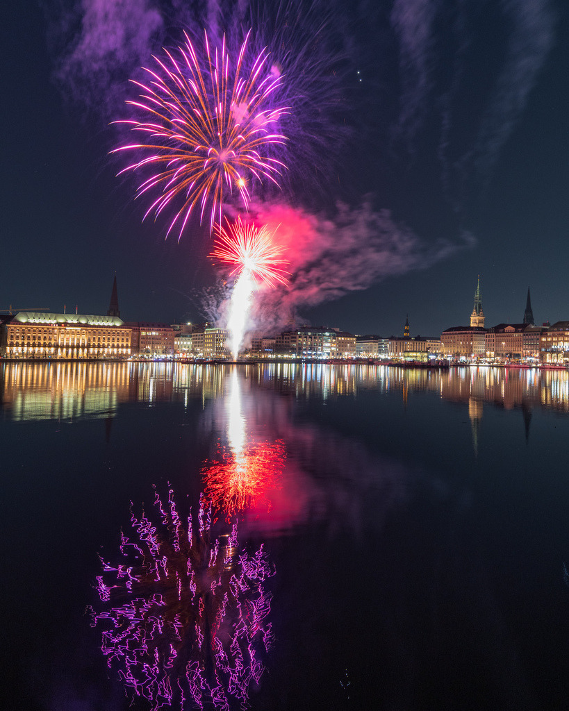 Farbenexplosion über der Alster | Intensiv pinkes und rotes Feuerwerk erhellt den Nachthimmel über Hamburg. Die kräftigen Farben spiegeln sich eindrucksvoll auf der dunklen Wasseroberfläche der Alster. - Realisiert mit Pictrs.com