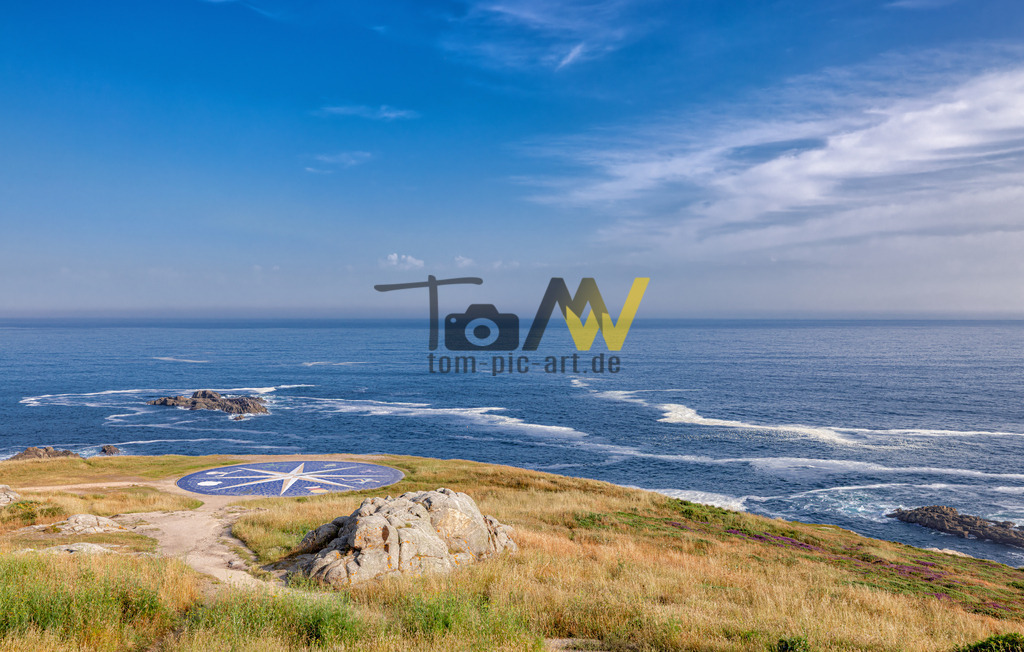 Kompassrose an der Küste  | Das Bild zeigt eine große, auf den Boden gemalte Kompassrose an einem Küstenort, bei der es sich wahrscheinlich um die "Rosa dos Ventos" (Windrose) in A Coruña, Galicien, Spanien, handelt. Eine Kompassrose ist ein grafisches Mittel zur Darstellung der Himmelsrichtungen und wird zur Orientierung auf geografischen Karten und Kompassen verwendet. Dieser spezifische Ort befindet sich in der Nähe des Herkulesturms (Torre de Hércules) in A Coruña. Die Region, Cabo Finisterre (Kap Finisterre), galt in der Römerzeit als das "Ende der Welt" ("Ende der Welt").  - Realisiert mit Pictrs.com