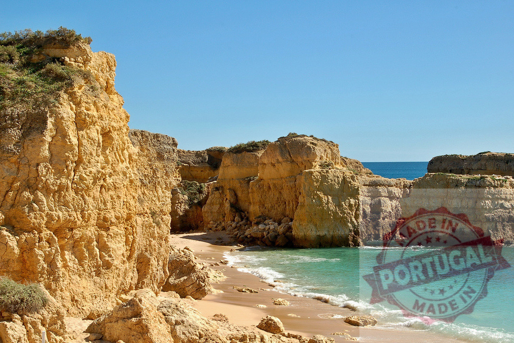 Algarve coastline with golden cliffs and turquoise ocean | Golden cliffs framing a sandy beach with crashing turquoise ocean waves under a clear blue sky - Realized with Pictrs.com