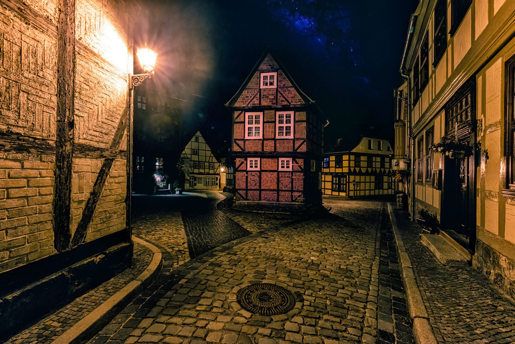 Fachwerkhaus in Quedlinburg bei Nacht--------Sternenhimmel | Das Bild zeigt eine historische Straße in Quedlinburg bei Nacht. Quedlinburg ist eine Stadt in Sachsen-Anhalt im Harzvorland. Die Stadt ist bekannt für ihre gut erhaltenen Fachwerkhäuser. Das historische Ensemble gehört zum UNESCO-Weltkulturerbe. Das gezeigte Bild vermittelt die nächtliche Atmosphäre der Altstadt mit ihren alten Gebäuden und der gepflasterten Straße. - Realisiert mit Pictrs.com