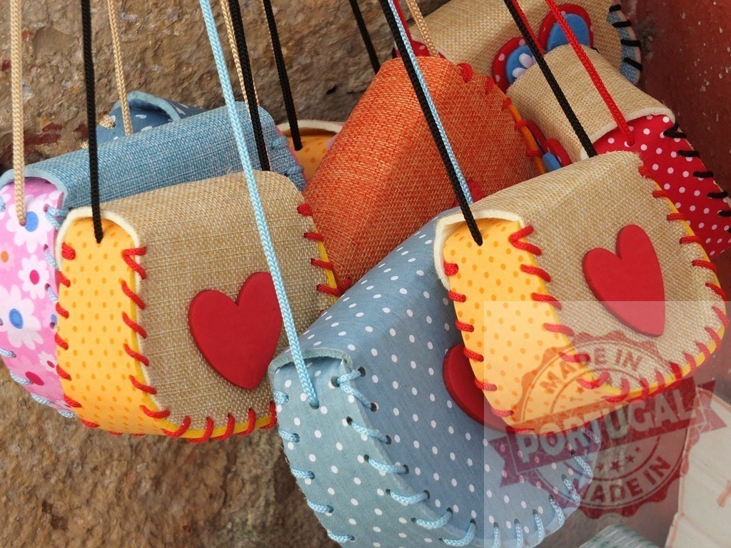 Colorful handmade fabric bags with red hearts hanging | Handmade fabric bags with cheerful patterns and red hearts displayed for sale - Realisiert mit Pictrs.com