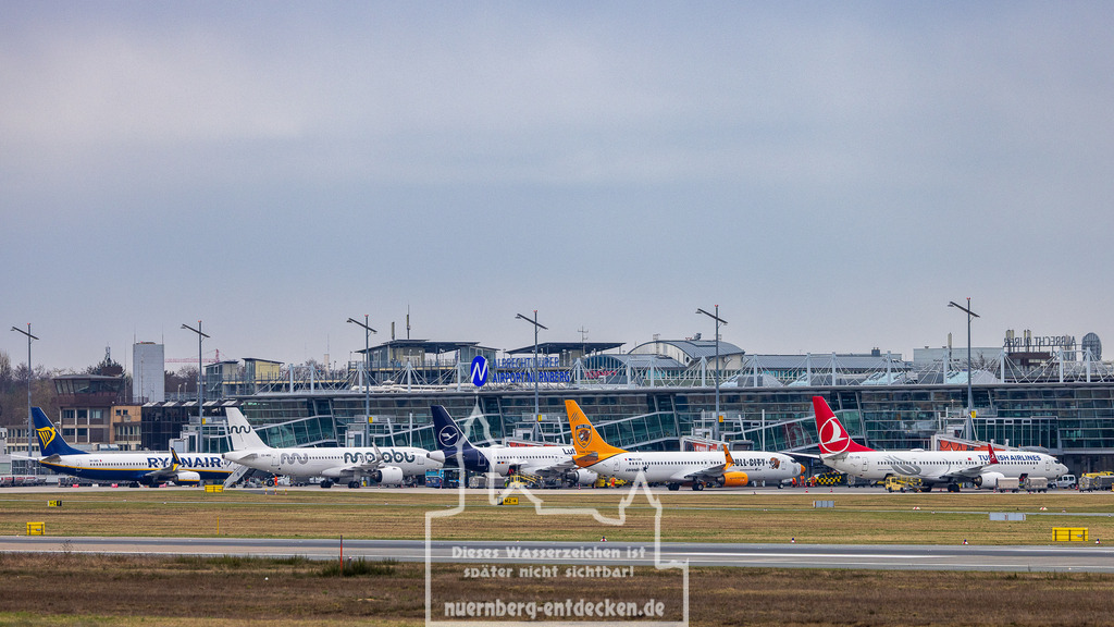 Flughafen Nürnberg, 30.03.2025 | Mehrere Passagierflugzeuge verschiedener Fluggesellschaften, darunter Ryanair, Marabu, Lufthansa, Corendon Airlines und Turkish Airlines, stehen auf dem Vorfeld des Albrecht-Dürer-Flughafens in Nürnberg. Im Hintergrund ist das Terminalgebäude mit dem Flughafenschriftzug zu sehen. - Realisiert mit Pictrs.com