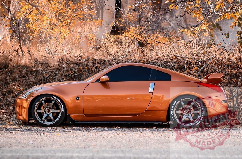Orange Nissan 350Z sports car parked roadside in autumn | Custom orange sports car parked on a road with autumn foliage and a rocky cliff background - Realisiert mit Pictrs.com