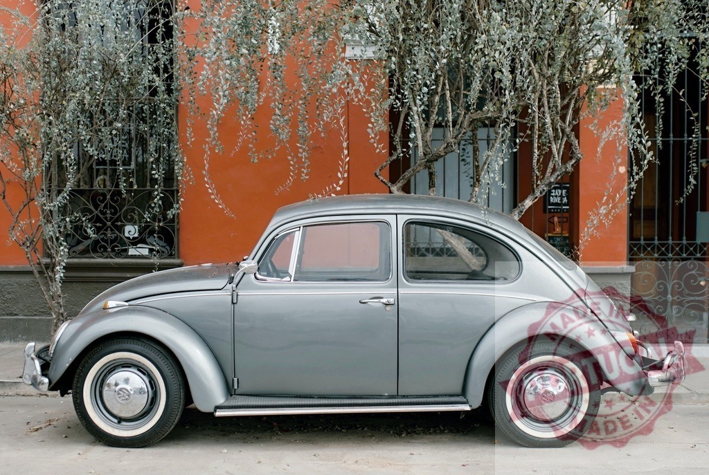 Volkswagen Beetle parking on street near orange wall | Classic gray Volkswagen Beetle car parked by an old building with a vibrant orange wall - Realized with Pictrs.com