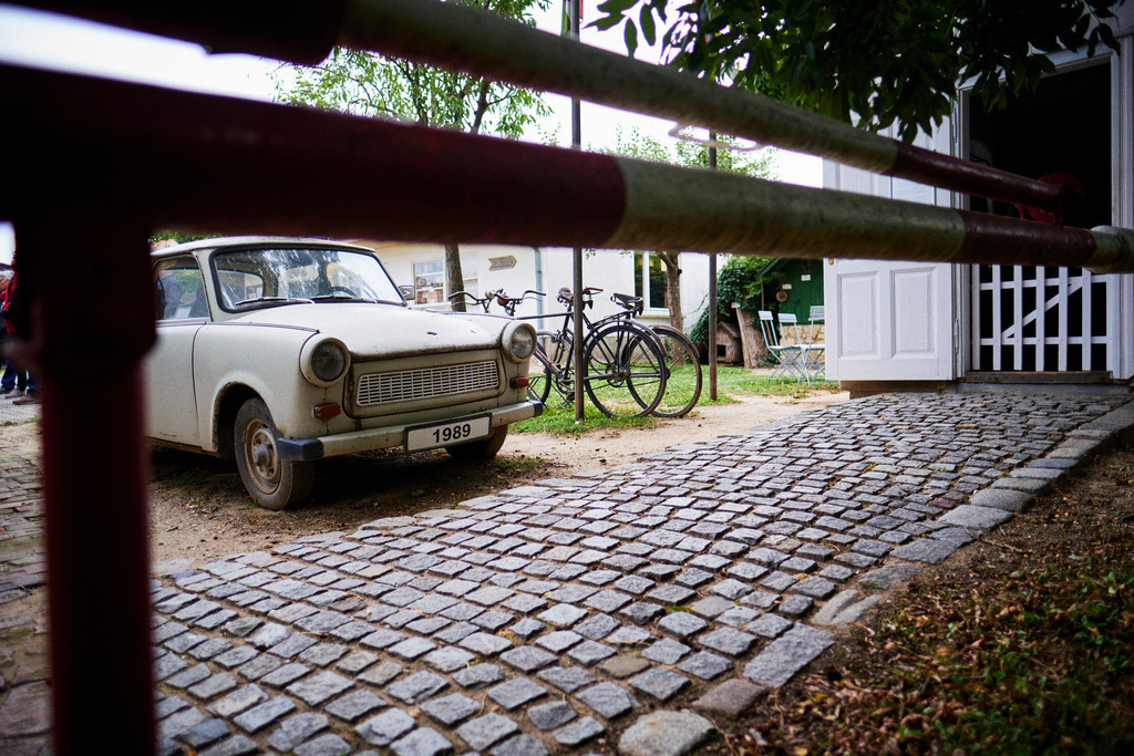 Trabi mit Blick auf eine Schranke und der Zollstation | Mönchhof, Austria - October 06, 2021: Dorfmuseum Mönchhof; Trabi mit Blick auf eine Schranke und der Zollstation. - Realisiert mit Pictrs.com