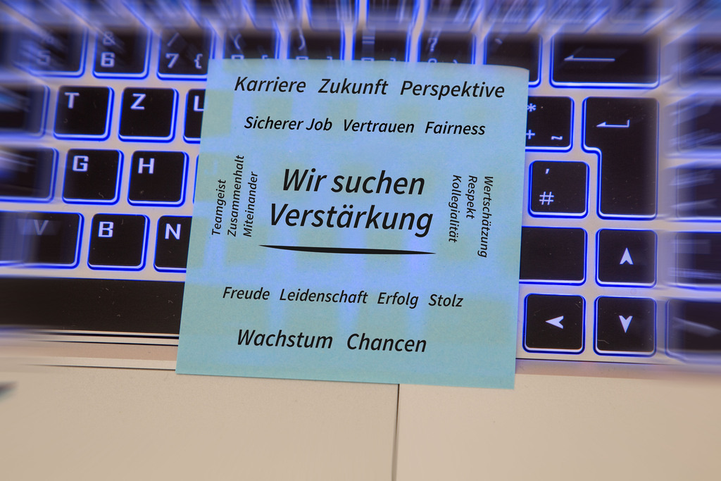 WIR SUCHEN VERSTÄRKUNG | (Hinzugefügter) Text WIR SUCHEN VERSTÄRKUNG, umgeben von positiven Begriffen wie Karriere, Zukunft, Teamgeist, Vertrauen, Wertschätzung, Wachstum und Chancen auf einem auf einem Laptop liegenden Zettel - Realisiert mit Pictrs.com