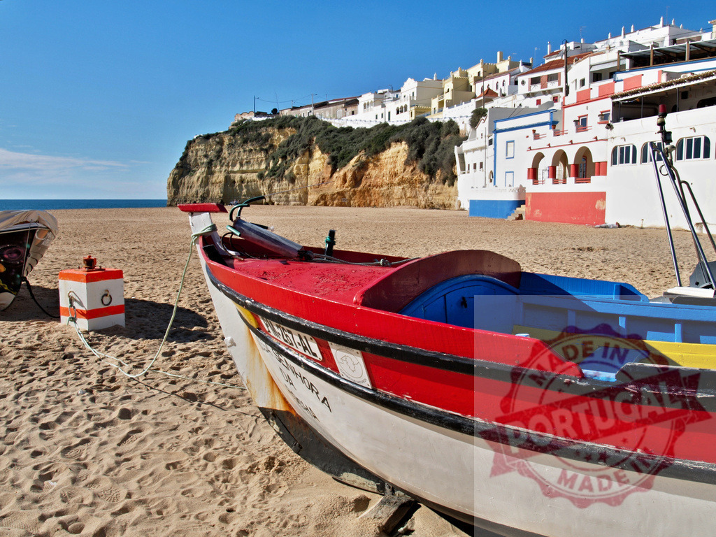 Fishing boat resting on Carvoeiro beach, Algarve Portugal | Traditional fishing boat drying on sandy beach with white village houses and cliff backdrop - Realized with Pictrs.com