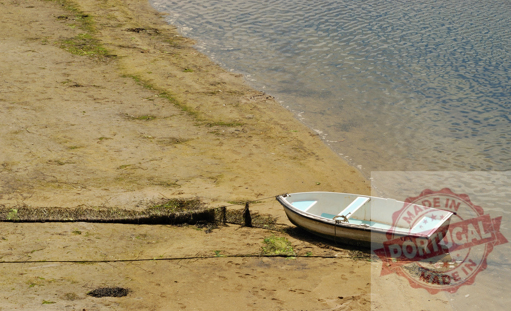 Small white boat pulled onto sandy shore near water. Galicia - Spain | Small boat resting on a sandy bank by calm water in daylight, tide is low - Realized with Pictrs.com