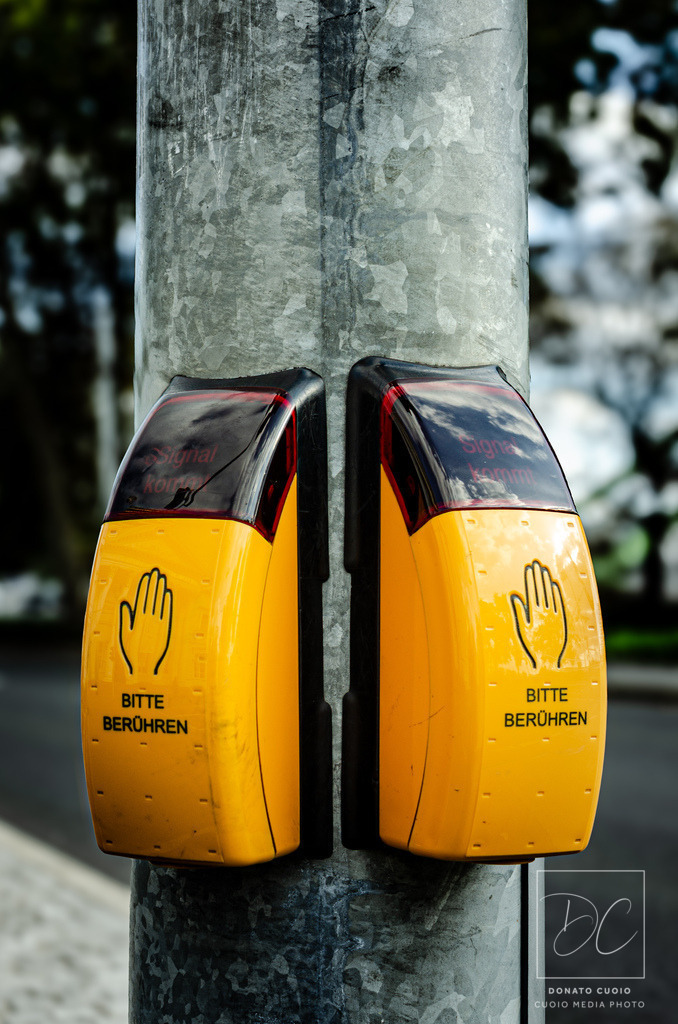"Bitte berühren" – Berührung, die den Verkehr lenkt | Ein sanfter Druck mit großer Wirkung: Die Fußgängerampel-Taster in leuchtendem Gelb mit der eindeutigen Aufforderung „BITTE BERÜHREN“ machen den Weg frei für eine sichere Straßenüberquerung. Doch diese Worte könnten mehr bedeuten – eine Einladung zur Interaktion, zur Verbindung mit der Umgebung. Die Taster sind nicht nur funktional, sondern auch ein Symbol dafür, wie eine einfache Berührung Veränderungen bewirken kann. Die Aufnahme zeigt diese modernen Anforderungstaster am Frankfurter Ufer (Nordseite) nahe dem Literaturhaus, wo Fußgänger den Straßenverkehr sicher und bequem überqueren können.  - Realisiert mit Pictrs.com