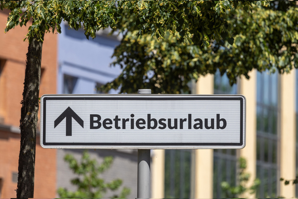 Betriebsurlaub - Schild in vor einem Bürogebäude mit der Aufschrift BETRIEBSURLAUB | (Fotomontage) Schild in vor einem Bürogebäude mit der Aufschrift BETRIEBSURLAUB - Realisiert mit Pictrs.com