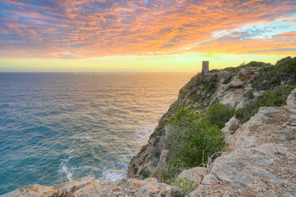 Sonnenuntergang am Cap Blanc auf Mallorca | Der Wachturm am Cap Blanc steht markant auf der schroffen Steilküste und bildet einen klaren Orientierungspunkt entlang der Südküste Mallorcas. Im gleichmäßigen Licht des Sonnenuntergangs treten die Strukturen des Mauerwerks und die Form der Felsabbrüche deutlich hervor. - Realisiert mit Pictrs.com