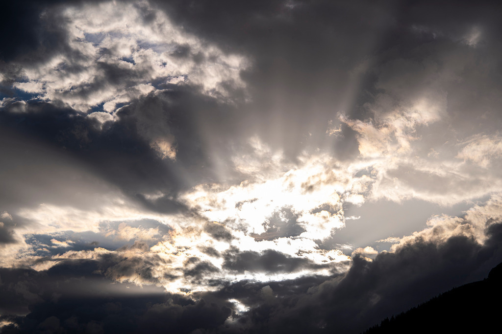 Spektakuläres Wolkenspiel: Dramatisches Lichtspektakel am Alpenhimmel | Ein faszinierender Naturschauspiel über Garmisch-Partenkirchen: Durch eine wuchtige, dunkle Wolkenwand bricht strahlendes Sonnenlicht in kraftvollen, fächerförmigen Strahlen hervor. Das Wechselspiel aus Licht und Schatten verleiht dem Himmel eine beinahe mystische Tiefe und Dynamik. Am unteren Bildrand zeichnet sich die schroffe Silhouette der oberbayerischen Bergwelt ab. Eine bildgewaltige Aufnahme, die die wilde Unberechenbarkeit des Wetters und die erhabene Magie der Alpen spürbar macht. - Realisiert mit Pictrs.com