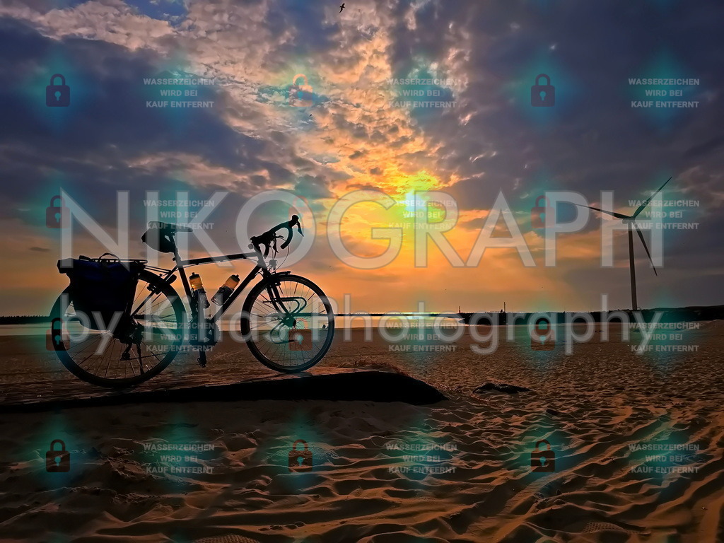 Randonneur’s Traum: Sonnenuntergang mit Blick auf Windrad und Mole | Ein idyllischer Abendhimmel über der Nordsee in Hvide Sande, Dänemark – ein perfekter Out-of-Home-Moment am Strand. Ein Randonneur hat sein Fahrrad mit Fahrradtasche an der Mole abgestellt, während die Sonne hinter den Wolken versinkt und den Sandstrand in warmes Licht taucht. Ein Windrad dreht sich sanft im Hintergrund – ein stilles Zeugnis der dänischen Küstenlandschaft. Wolkenhimmel, Nordsee, Idylle: alles vereint in einem Bild, das Ruhe, Verkehrswende, Endergiewende, Natur und Weite vermittelt.Möchten Sie dieses Motiv als Fotoprodukt (z. B. Leinwand, Poster, Kalender) erwerben? Besuchen Sie nikograph.eu – dort können Sie individuelle Fotoprodukte bestellen und die Stimmung dieses Sonnenuntergangs in Ihrem Zuhause festhalten.