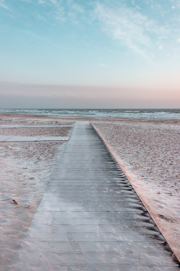 Wandbild: Weg am Sandstrand in dezenten Farben | Dieses Wandbild im Hochformat zeigt einen Weg am Strand in einer wunderschönen Morgenstimmung. Der Weg führt fast direkt bis an die Wellen und bringt damit eine Tiefenwirkung ins Bild. Das Bild hat einen sehr geringen Farbumfang. Im unteren Bereich des Bildes ist durch den Sandstrand ein schöner natürlicher Sandton zu sehen. Neben dem Sandstrand bringen die leicht rötlichen Wolken am hellblauen Himmel Wärme ins Wandbild. Dieses Wandbild ist als Leinwand, als Acrylglas und Aluminium-Platte in vielen Abmessungen erhältlich. Holen Sie sich jetzt Urlaubsfeeling mit pastellartigen Farben für Ihr Zuhause. Ideal fürs Wohnzimmer, Schlafzimmer, Küche aber auch für das Büro oder die Praxis. - Realisiert mit Pictrs.com