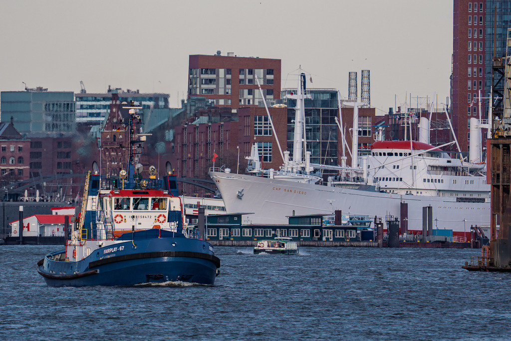 Schlepper FAIRPLAY-67 vor der Cap San Diego | Der Schlepper FAIRPLAY-67 bei der Fahrt hafenaufwärts. Im Hintergrund liegt der weiße Stückgutfrachter Cap San Diego an seinem Liegeplatz an der Überseebrücke. - Realisiert mit Pictrs.com