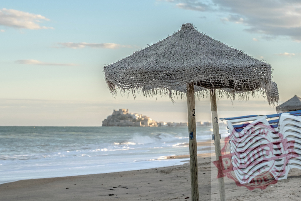 Peñíscola beach parasol and stacked chairs during off season | Beach parasol and stacked loungers on Peñíscola beach looking out to sea with a castle on the horizon - Realisiert mit Pictrs.com