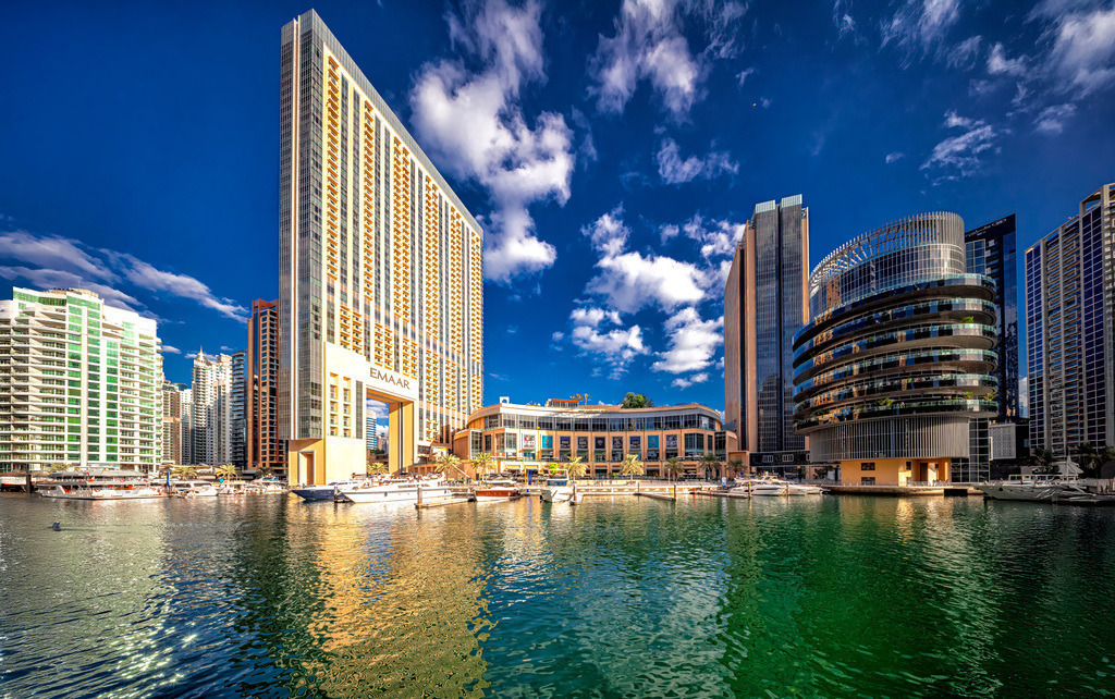Die Dubai Marina in den Vereinigten Arabischen Emiraten,Yachthafen | Das Bild zeigt die Dubai Marina in den Vereinigten Arabischen Emiraten, einen künstlich angelegten Yachthafen mit zahlreichen Wolkenkratzern. Lage: Der Stadtteil befindet sich etwa 25 Kilometer südwestlich des Stadtzentrums von Dubai. Gebäude: Im Zentrum ist das Gebäude der EMAAR Properties zu sehen, bekannt für luxuriöse Entwicklungen in der Region. Atmosphäre: Das Viertel ist bekannt für seine lebendige Promenade, gehobene Einkaufsmöglichkeiten und eine internationale Atmosphäre. Entwicklung: Die Marina wurde zwischen 2007 und 2017 erbaut und umfasst über 200 Hochhäuser.  - Realisiert mit Pictrs.com