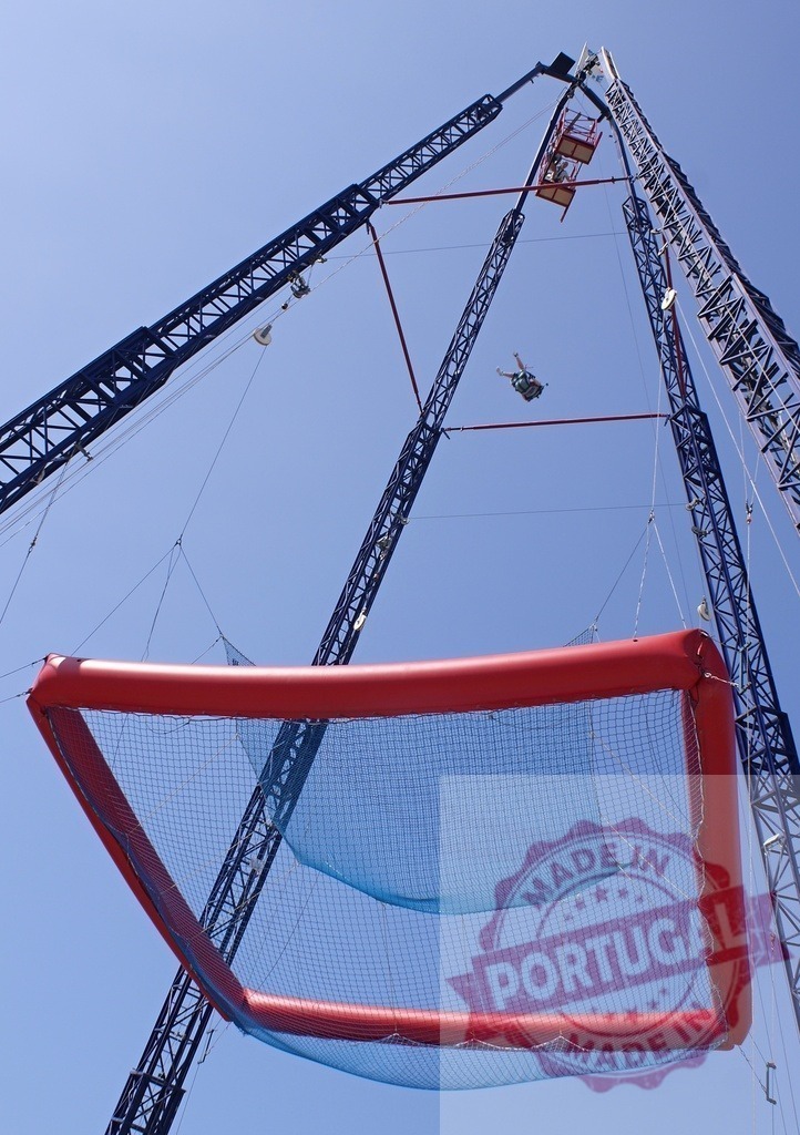 Person free falling during extreme amusement park SCAD dive | Person experiencing free fall from a high platform into a large safety net against a blue sky - Realisiert mit Pictrs.com