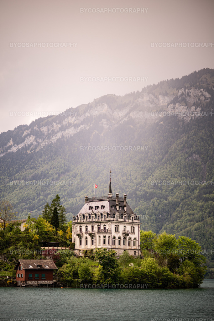 The Castle of Iseltwald _ Swiss Dreamland | Ein atemberaubendes Porträt eines der bekanntesten Wahrzeichen der Schweiz am Seeufer.Das elegante Schloss Iseltwald erhebt sich über dem türkisfarbenen Wasser des Brienzersees, umrahmt von nebelverhangenen Bergen und üppigem Frühlingsgrün.Sanftes Licht und ein zarter Pastellhimmel schaffen eine romantische, fast märchenhafte Atmosphäre – perfekt für jedes Zuhause, das Ruhe, Luxus und natürliche Eleganz ausstrahlen möchte.Ideal für Wohnzimmer, Schlafzimmer, Büros oder Hotelzimmer.Dieser Druck bringt ein Gefühl von Schweizer Ruhe und märchenhafter Landschaft in jedes Interieur. - Realisiert mit Pictrs.com