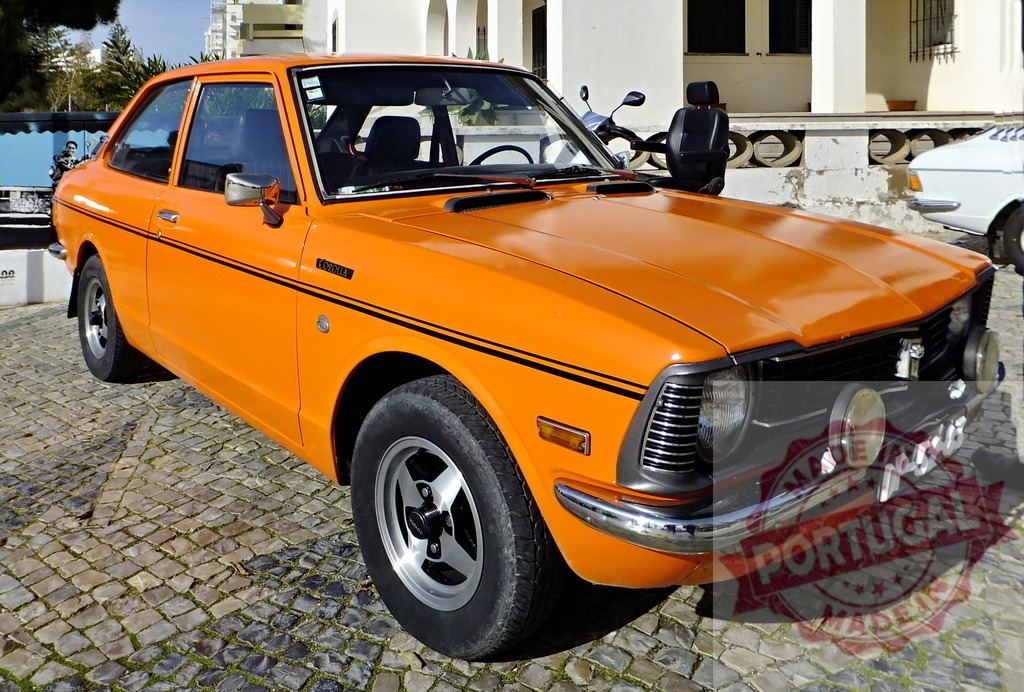 Orange Toyota Corolla parked on cobblestone street | Classic orange Toyota Corolla parked on a cobblestone street, showcasing its vintage design - Realized with Pictrs.com