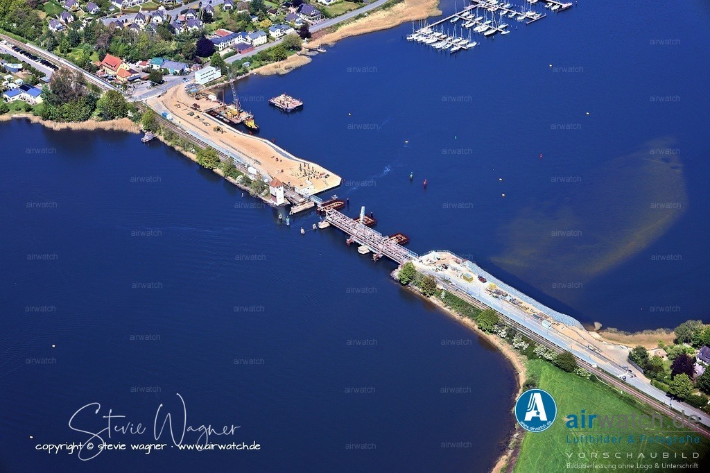 Luftbild Ostseefjord Schlei, Boren-Lindaunis Schleibrücke, Campingplatz Lindaunis, Sportboothafen Lindaunis | Die Lindaunisbrücke ist eine Straßen- und Eisenbahnklappbrücke, die den Meeresarm Schlei an einer seiner schmalsten Stellen überspannt. Die Brücke liegt im Gemeindeteil Lindaunis der Gemeinde Boren in Schleswig-Holstein. Seit 2021 ist die Brücke für Eisenbahnen und Kraftfahrzeuge gesperrt. Sie kann seitdem nur noch zu Fuß überquert werden. Die Brücke wird abgebaut und durch einen Neubau ersetzt. Im März 2025 wurde eine Fertigstellung im Jahr 2027 für möglich gehalten