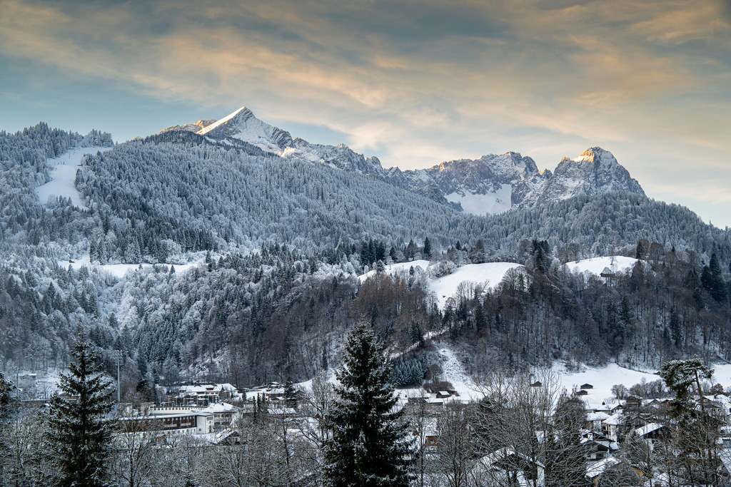 Winterzauber im Wettersteingebirge | Diese eindrucksvolle Aufnahme fängt die winterliche Pracht des Wettersteingebirges ein. Im Vordergrund erstreckt sich eine schneebedeckte Landschaft, gesäumt von dichten Nadelwäldern. Die imposanten Berggipfel, von der markanten Alpspitze über die majestätische Zugspitze bis hin zu den markanten Waxensteinen, ragen majestätisch in den klaren Winterhimmel. Die Sonne taucht die Landschaft in ein sanftes, warmes Licht und erzeugt faszinierende Schattenwürfe. Die Aufnahme vermittelt ein Gefühl von Ruhe und Erhabenheit und lädt dazu ein, die Schönheit der Natur zu genießen. - Realisiert mit Pictrs.com