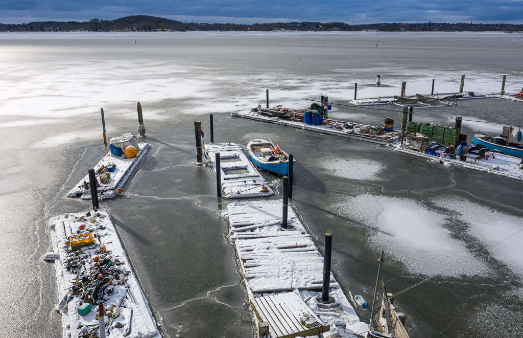 2021-008 | Im Eis der Schlei: Landungsbrücken und Boote in der Fischersiedlung Holm in Schleswig aus der Vogelperspektive - Realisiert mit Pictrs.com