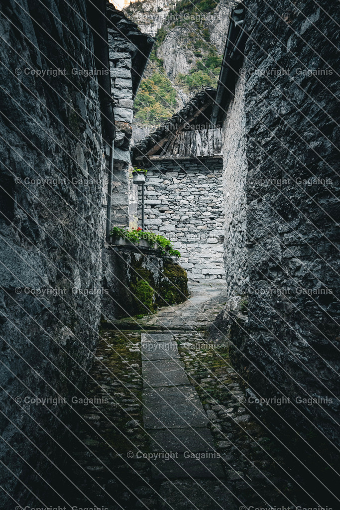 Foroglio Gasse | Foroglio ist ein malerisches Bergdorf im Bavonatal im Tessin, Schweiz. Es ist bekannt für seinen beeindruckenden Wasserfall, der rund 80 Meter tief in das Tal stürzt, sowie für seine traditionellen Steinhäuser, engen Gassen und unberührte alpine Landschaft. Das Dorf wirkt wie aus einer anderen Zeit und zieht Natur- und Fotoliebhaber gleichermaßen an.