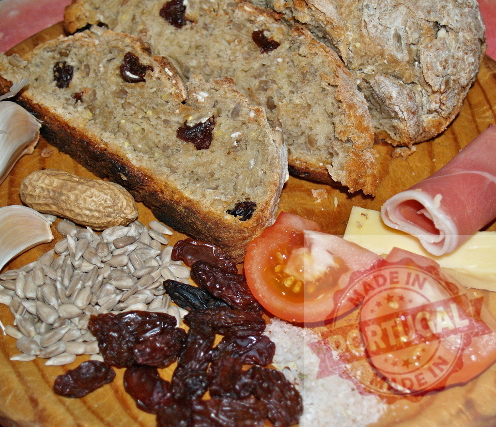 Rustic bread slices and gourmet snack board | Rustic bread slices with raisins, prosciutto, cheese, tomatoes, and other appetizers on a wooden board - Realisiert mit Pictrs.com