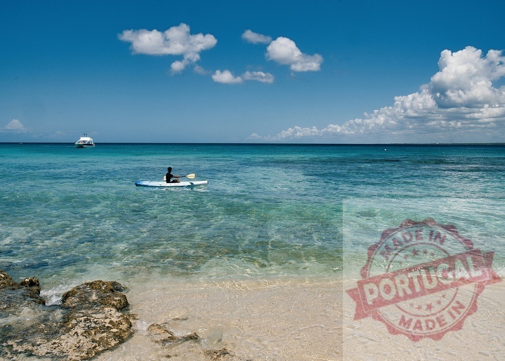 Person kayaking in turquoise Caribbean Sea water | Kayaker paddling in clear blue ocean water under a sunny sky near the beach - Realized with Pictrs.com