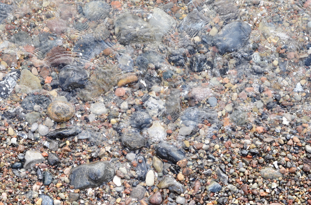 Strandboden mit Steinen im Wasser | Der Übergang zwischen Strand und Wasser wird als Küste beschrieben - Realisiert mit Pictrs.com