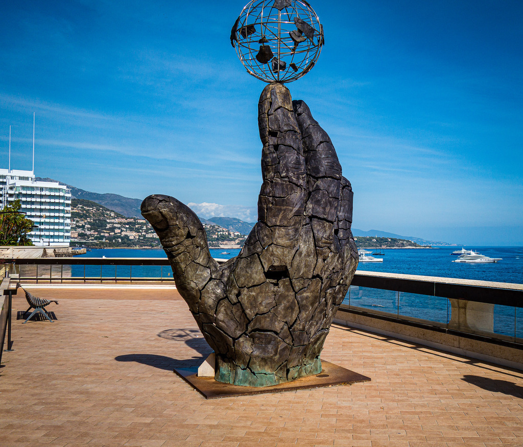 Wandbild Kunstdruck Poster – Monaco Hand Sculpture: Moderne Kunst am Mittelmeer | Hol dir die majestätische Kunst und das luxuriöse Flair der französischen Riviera direkt in deine Wohnräume. Diese beeindruckende Fotografie fängt eine monumentale Outdoor-Hand-Skulptur im Fürstentum Monaco ein. Das zeitgenössische Kunstwerk hebt sich imposant vor der tiefblauen Bucht, den Luxusyachten im Hafen und den charakteristischen Hängen der Côte d'Azur ab. Das harmonische Zusammenspiel aus rauer, gemeißelter Textur und der endlosen maritimen Weite versprüht pure Eleganz und exklusives Urlaubsflair.Dieses moderne und ausdrucksstarke Motiv ist der perfekte, kunstvolle Blickfang für ein stilvolles Büro, das repräsentative Wohnzimmer, ein helles Design-Loft oder für eine elegante Atmosphäre im Flur.Um die feinen Strukturen des Steins und die immense Leuchtkraft des Mittelmeer-Blaus perfekt in Szene zu setzen, empfehle ich den Druck auf unseren Premium-Materialien: Erlebe kinoreife Tiefenwirkung auf edlem Acrylglas, hochmoderne Eleganz auf robustem Alu-Dibond oder einen klassischen Galerie-Charakter auf einer matten Leinwand. Bring exklusiven Riviera-Lifestyle an deine Wand! - Realisiert mit Pictrs.com