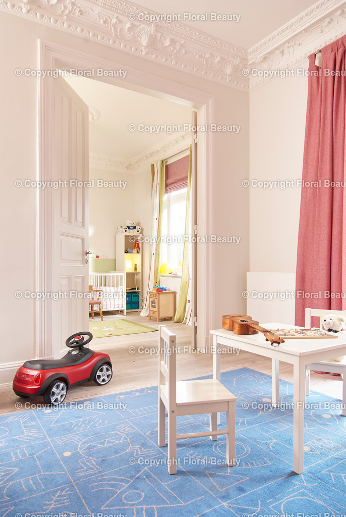 Kinderzimmer im Altbau mit Durchgang | Kinderzimmer mit blauem Teppich, Tischchen und rotem Rutscheauto. Durchgang in weiteres Kinderzimmer. Stuck an der Decke. - Realisiert mit Pictrs.com