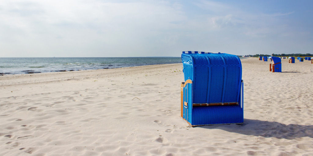Panorama Wandbild: Strandkörbe am Weidefelder Strand | Dieses Panorama Wandbild zeigt einen wunderschöner Tag am Sandstrand von Weidefeld, an dem die Sonne auf die blauen Strandkörbe und den warmen Sand scheint. Die Farben des Strandes und des Himmels sorgen für eine entspannte und friedliche Atmosphäre. Man kann fast das sanfte Rauschen der Wellen hören und die frische Meeresbrise spüren. - Realisiert mit Pictrs.com