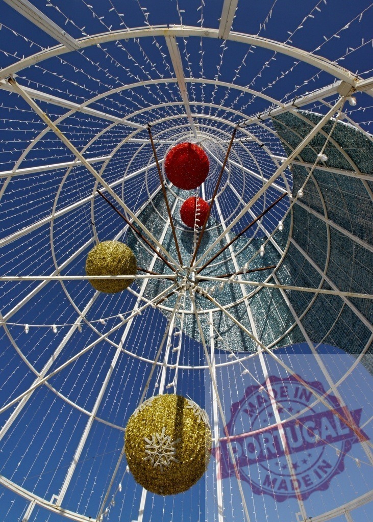 Giant metal christmas tree with hanging balls and lights against blue sky | Low angle view of christmas decorations hanging from a giant metal christmas tree against blue sky - Realisiert mit Pictrs.com