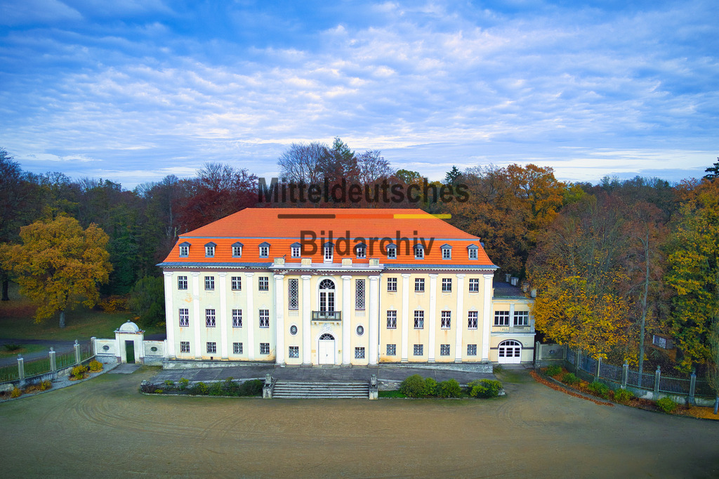 Schloß-Tangerhütte_0005 | Das Luftbild zeigt das Neue Schloss Tangerhütte an einem sonnigen Herbsttag aus einer sehr tiefen Drohnenperspektive. Durch die geringe Flughöhe rückt die eindrucksvolle Architektur des Schlosses besonders nah in den Vordergrund und ermöglicht einen detaillierten Blick auf die reich gestalteten Fassaden, Türme, Erker und Dachlandschaften des historistischen Bauwerks. Die Aufnahme vermittelt die Wirkung des Schlosses aus einer Perspektive, die seine Größe und architektonische Vielfalt eindrucksvoll zur Geltung bringt.Umgeben wird das Schloss von den farbenprächtigen Bäumen des weitläufigen Schlossparks. Die herbstliche Vegetation präsentiert sich in leuchtenden Gelb-, Orange- und Rottönen und bildet einen reizvollen Kontrast zu den hellen Fassaden und den dunklen Dächern der Anlage. Die bunten Baumkronen rahmen das Schloss ein und verleihen der Aufnahme eine besonders stimmungsvolle Atmosphäre.Über der Szenerie spannt sich ein strahlend blauer Himmel, der die klaren Konturen des Bauwerks zusätzlich betont und für ausgezeichnete Sichtverhältnisse sorgt. Das warme Herbstlicht hebt die architektonischen Details hervor und lässt die Farben der Natur besonders intensiv erscheinen. Durch die Nähe der Drohne entsteht ein außergewöhnlich plastischer Eindruck der Schlossanlage, während gleichzeitig Teile des historischen Parks sichtbar bleiben.Die Aufnahme dokumentiert das Neue Schloss Tangerhütte als eines der bedeutendsten Schlossbauwerke der Altmark. Die Kombination aus niedriger Drohnenperspektive, herbstlicher Parklandschaft und wolkenlosem Himmel macht das Bild zu einer eindrucksvollen Darstellung dieses architektonischen Kleinods, das sich harmonisch in die historische Gartenanlage einfügt und bis heute das Zentrum des Tangerhütter Schlossparks bildet. - Realisiert mit Pictrs.com
