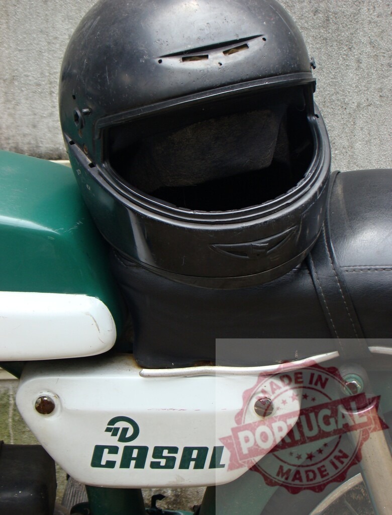 Black helmet resting on a vintage Casal moped | Old black helmet placed on the seat of a vintage green and white Casal moped - Realisiert mit Pictrs.com