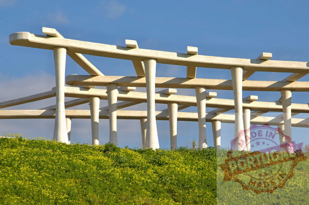 Concrete brutalist architecture structure against blue sky. Espana - Cadiz | Concrete brutalist geometric structure standing on a green grassy hill under a clear blue sky - Realized with Pictrs.com