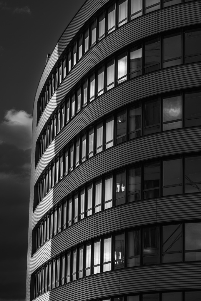 Curved Silence | Curved Silence zeigt die ruhige Kraft moderner Architektur in ihrer reinsten Form.Die geschwungene Fassade, die präzisen Linien und das Spiel aus Licht, Schatten und Reflexionen verleihen dem Gebäude eine fast skulpturale Wirkung.In monochromer Darstellung reduziert sich die Szene auf Struktur, Form und Atmosphäre – genau dort, wo urbane Architektur ihre stärkste visuelle Sprache entfaltet.Dieses Fine-Art-Motiv steht für Klarheit, Eleganz und zeitlose Urbanität und eignet sich besonders für moderne Wohnräume, Büros und designorientierte Interieurs. - Realisiert mit Pictrs.com