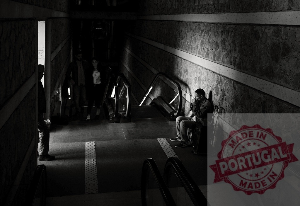 Man feeling solitary in subway station with escalators | Man sitting alone against a textured wall in a dark subway station with other people passing - Realisiert mit Pictrs.com